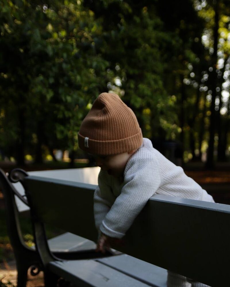Et lite barn med brun lue som klatrer ved en benk i parken